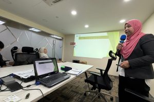 A woman holding a microphone in front of a laptop